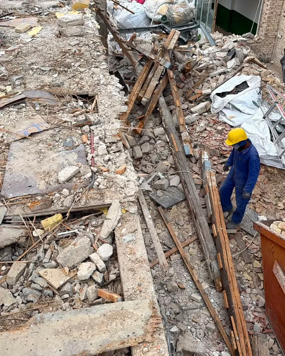Blick über eine Abbruchbaustelle: gebrochener Beton, ausgebaute Holzbalken und gefüllte Big-Bags, dazwischen ein Arbeiter mit gelbem Helm.