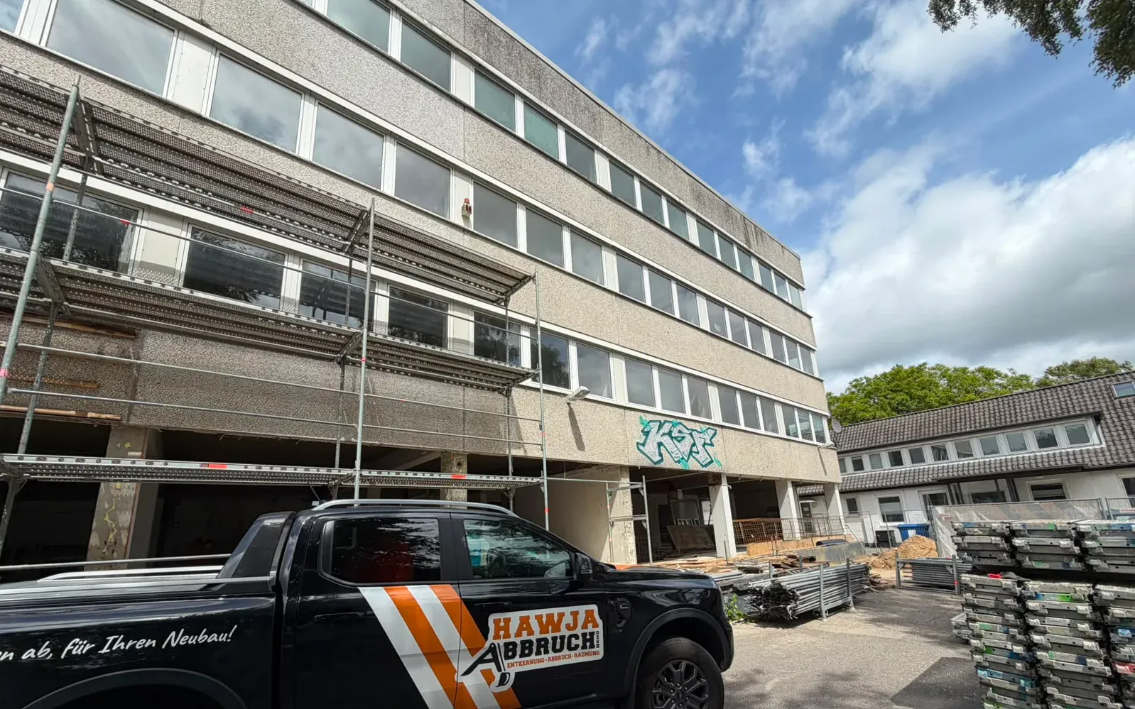 Vierstöckiges Verwaltungsgebäude mit Gerüst und Bauzaun, davor ein beschriftetes Fahrzeug der Hawja Abbruch GmbH.