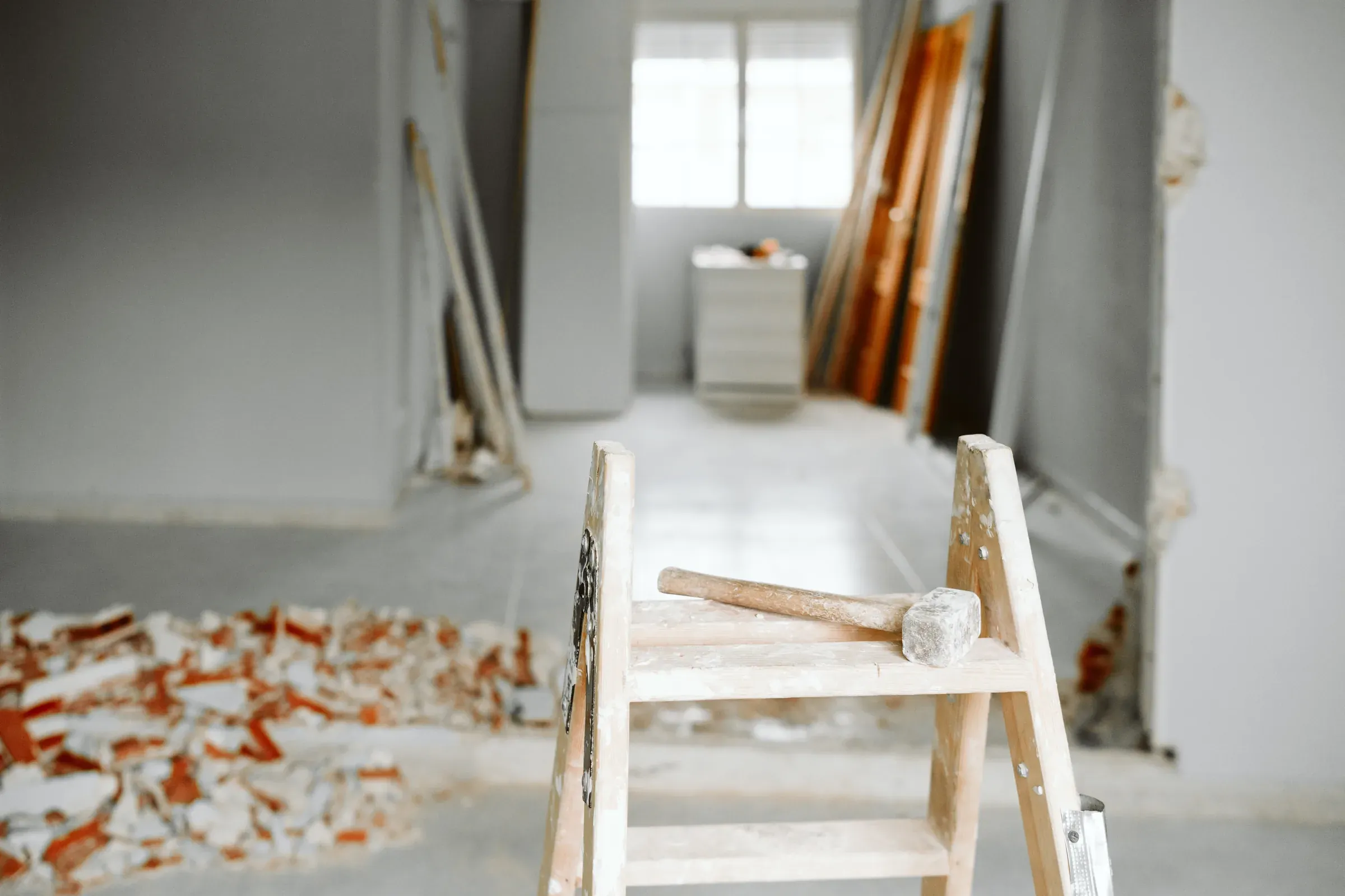 Bis auf den Rohbau zurückgebaute Wohnung: Putz teilweise abgeschlagen, Ziegelbruch auf dem Estrich, ein Fäustel liegt auf einer Trittleiter.