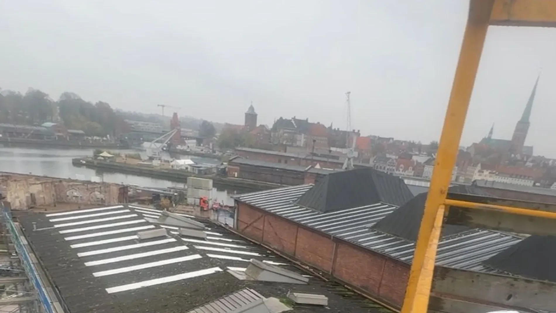 Blick von einer Baustelle über die Trave auf Lübeck: alte Hafenkräne, Speichergebäude und die Türme der Altstadt.