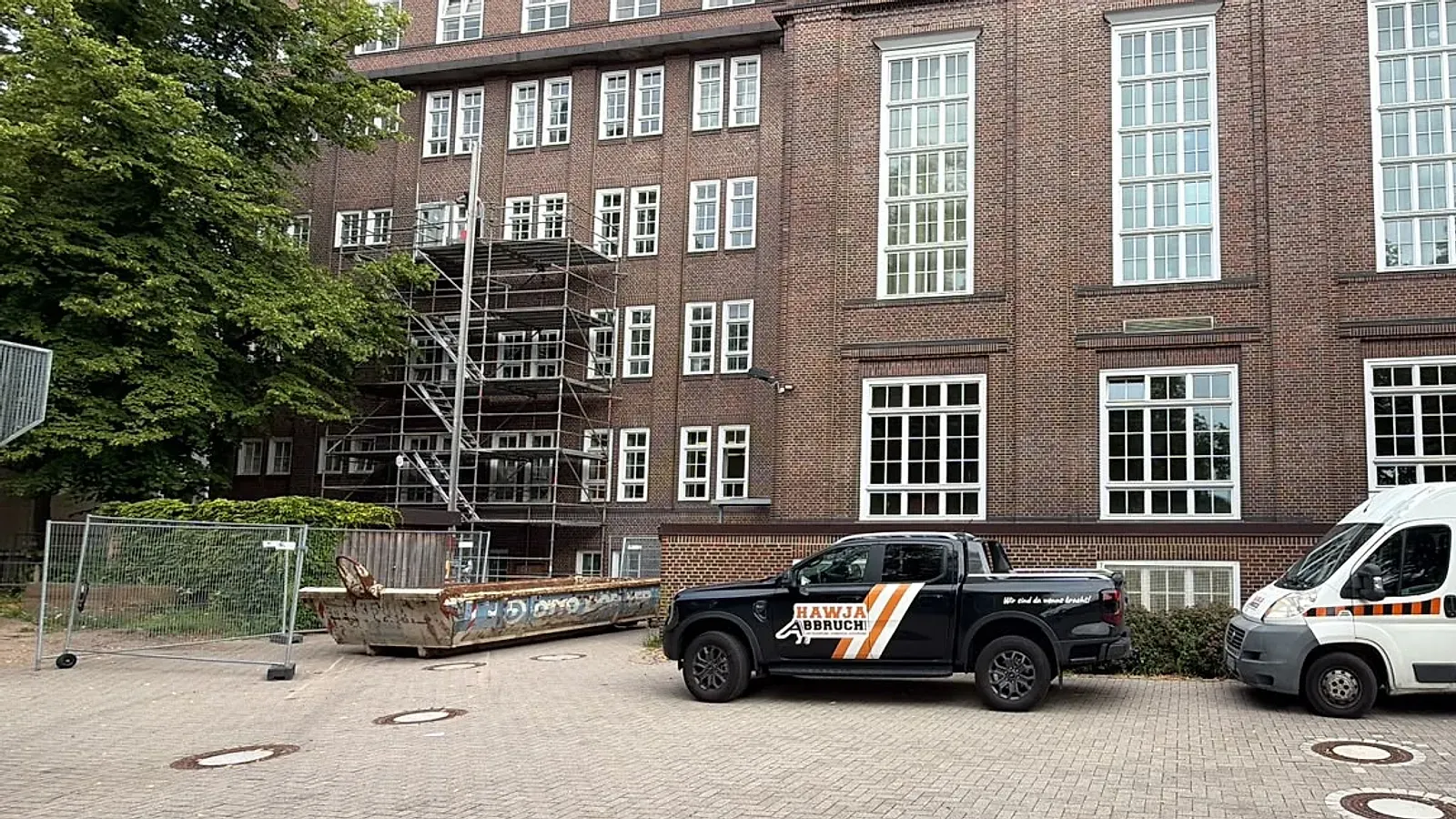 Beschriftete Fahrzeuge der Hawja Abbruch GmbH vor einem Backsteingebäude, an dem gearbeitet wird.