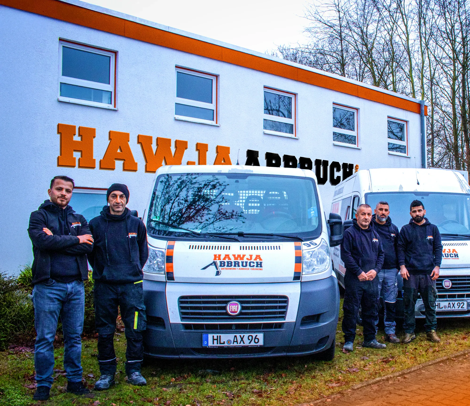 Ein Teil des Hawja-Teams vor dem Betriebsgebäude in der Spenglerstraße, daneben drei beschriftete Firmenfahrzeuge.